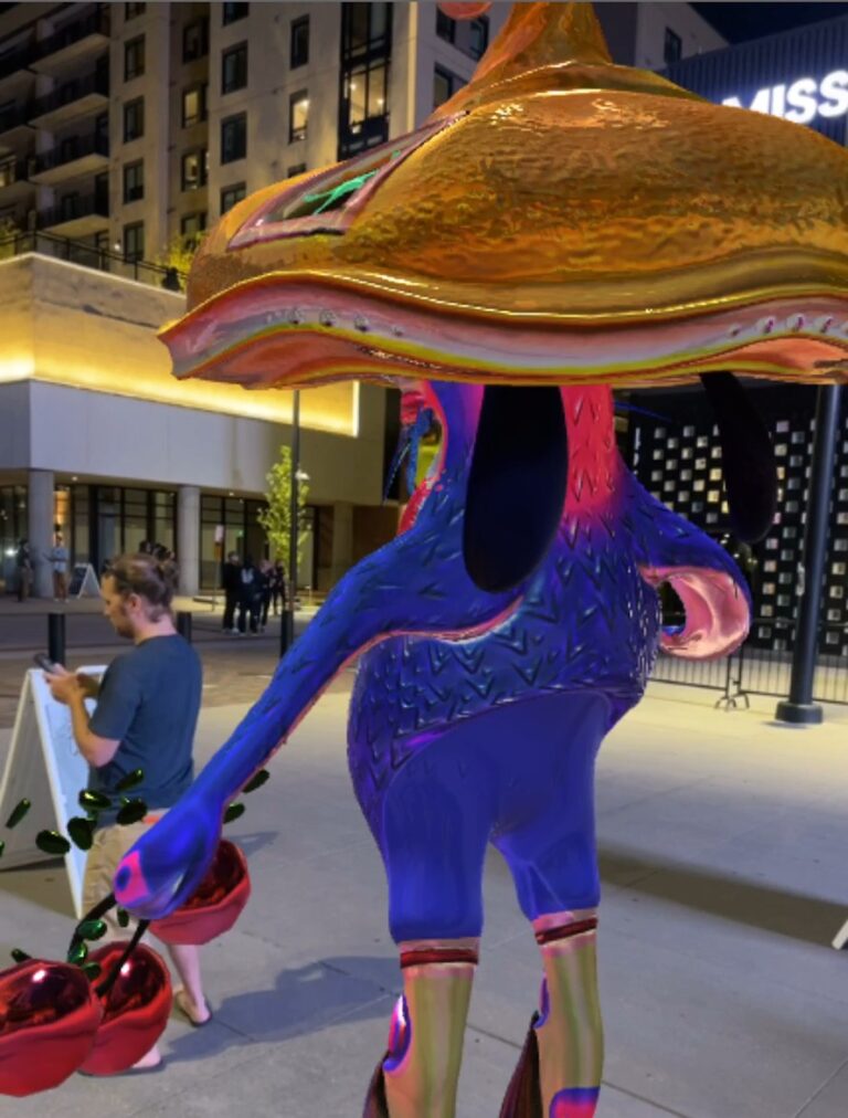 A visitor stands at a QR code sign beside a large AR bird-like creature wearing a mushroom hat, outside Mission Ballroom at night