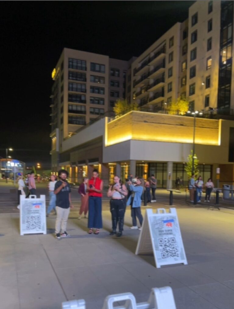 Visitors gather at night beside QR code signs that mark AR sculpture stops outside Mission Ballroom in Denver