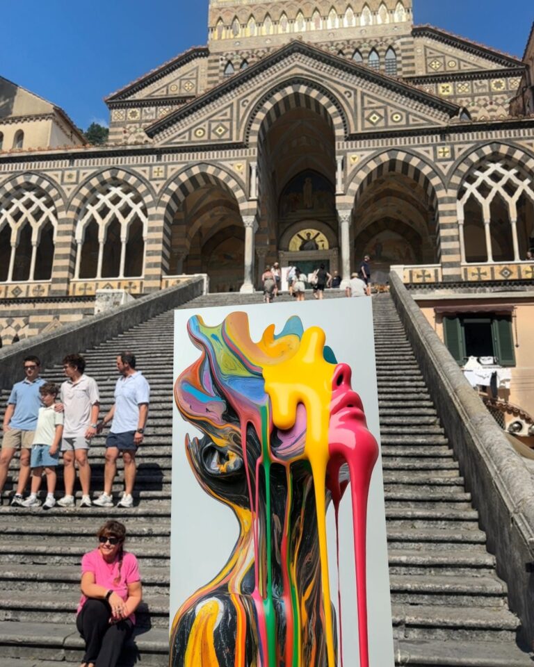 A colorful painted face by Archana Aneja standing in augmented reality on the steps of Amalfi Cathedral, with visitors sitting nearby