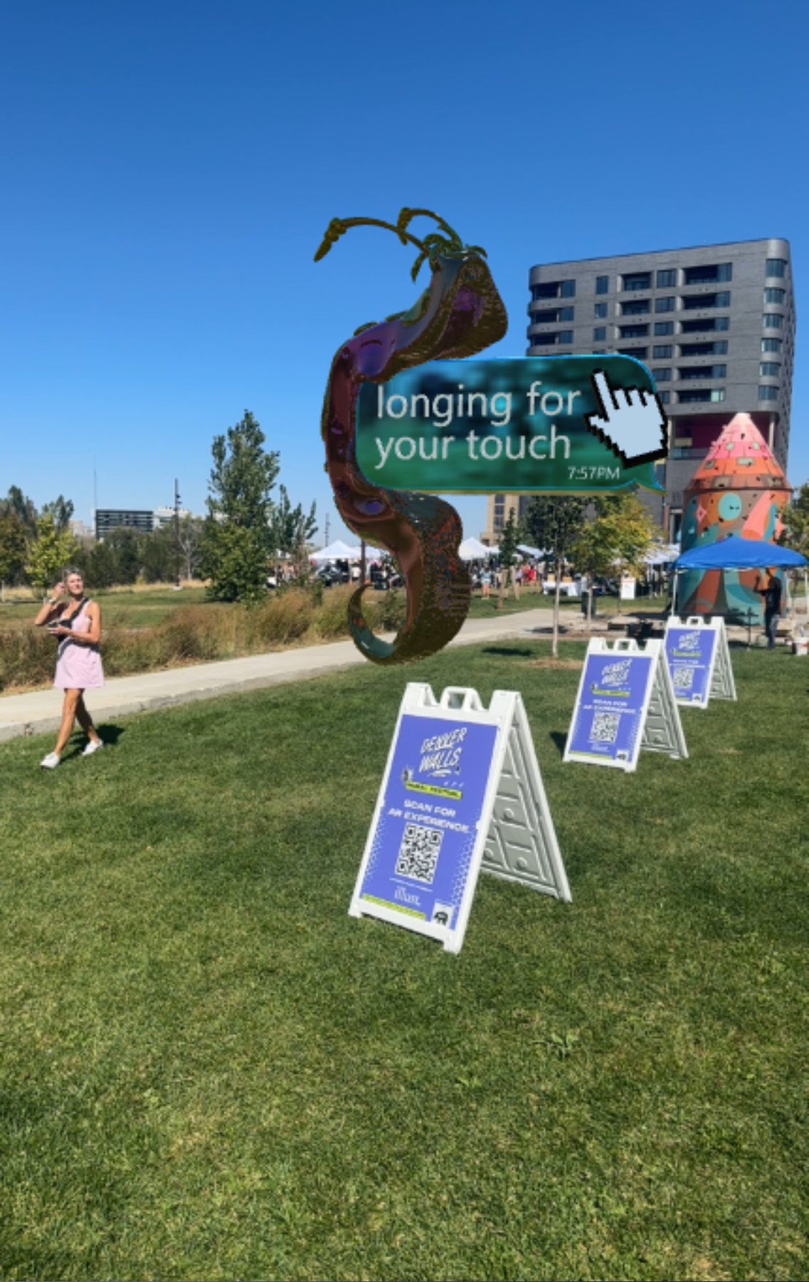 An AR sculpture with a speech bubble beside event signs and visitors in a Denver park, viewed with illust